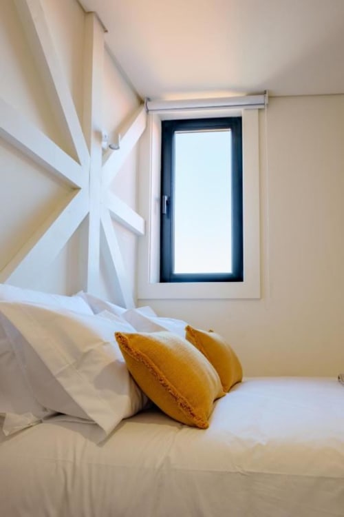 Quarto claro com arte geométrica branca, almofadas ocre na cama e janela com moldura preta no duplex AgapeStay Porto