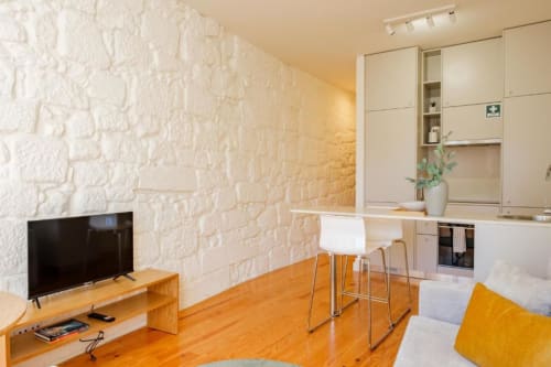 Apartamento moderno no Porto com paredes em pedra branca, assoalho em madeira, kitchenette, zona de refeições e TV