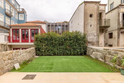 Pátio do AgapeStay Porto com gramado verde, muros de pedra e edifício com porta vermelha no Porto, Portugal