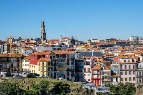Edifícios coloridos no centro histórico do Porto com telhados de terracota e torre da igreja sob céu azul