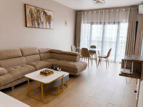 Modern apartment living room with beige sectional sofa, dining area, and city view at DakarByDays hotel in Dakar