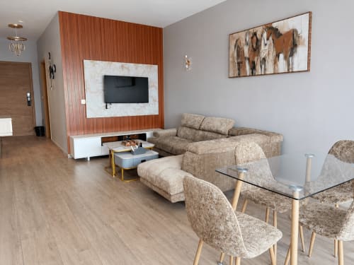 Modern living room at DakarByDays apartment with beige sofa, TV wall, and wooden floors in Dakar