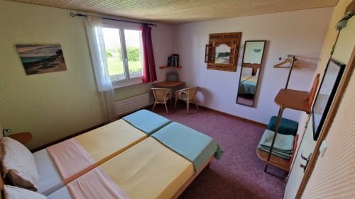 Chambre twin avec vue sur la rivière à l'Hôtel Rose, Beauvoir. Mobilier en bois, moquette violette, bureau et équipements modernes.