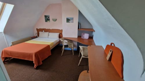 Chambre mansardée douillette à l'Hôtel Rose à Beauvoir avec lit en bois, accents orange, bureau et plafond en pente