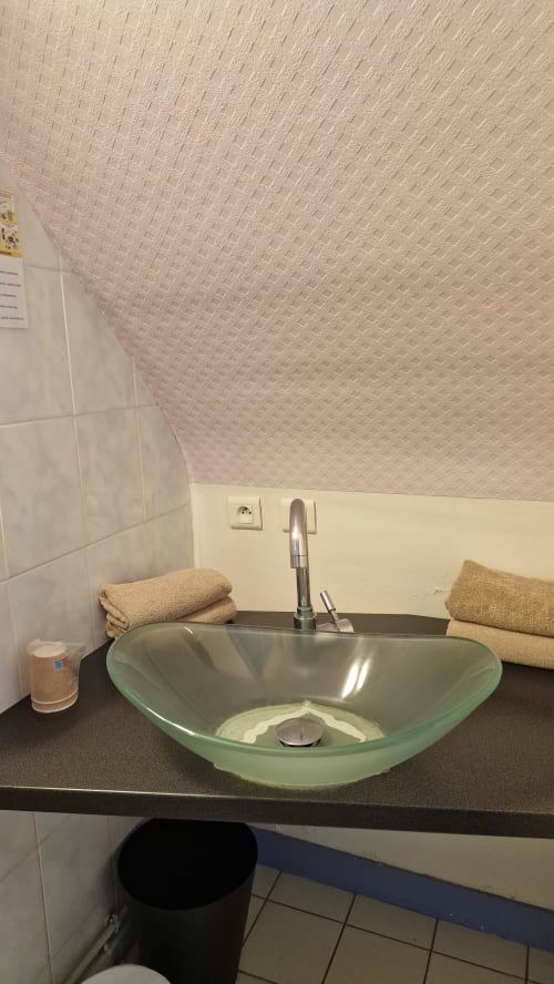 Lavabo en verre vert moderne avec robinet chromé dans la salle de bains de l'Hôtel Rose à Beauvoir, avec serviettes et papier peint rose texturé