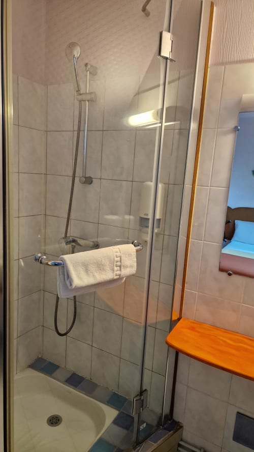 Cabine de douche moderne en verre avec douchette et serviette blanche à l'Hôtel Rose, Beauvoir