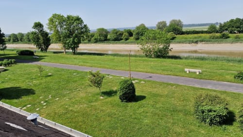 Vue sereine sur la rivière depuis l'Hôtel Rose à Beauvoir, France, avec pelouse verte, arbres et allée pavée le long de l'eau
