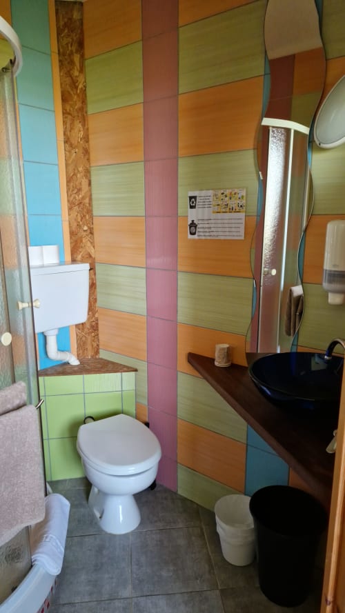 Salle de bains colorée à l'Hôtel Rose à Beauvoir avec carrelage multicolore, toilettes blanches, lavabo noir et miroir
