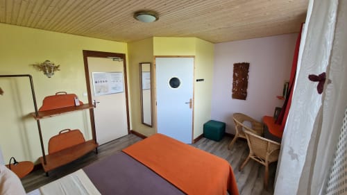 Chambre double cosy à l'Hôtel Rose de Beauvoir avec literie orange, mobilier en bois et vue sur la rivière