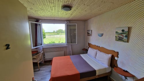 Chambre double avec vue sur la rivière à l'Hôtel Rose, Beauvoir. Lit en bois, literie colorée, papier peint à motifs, fenêtre