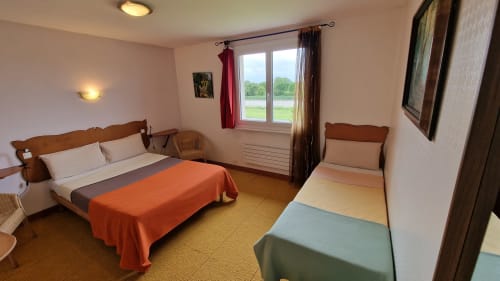Chambre triple avec vue sur la rivière à l'Hôtel Rose à Beauvoir, avec lits double et simple, fenêtre donnant sur la verdure