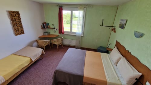 Chambre triple avec vue sur la rivière à l'Hôtel Rose, Beauvoir. Deux lits à têtes en bois, bureau, murs verts et jardin