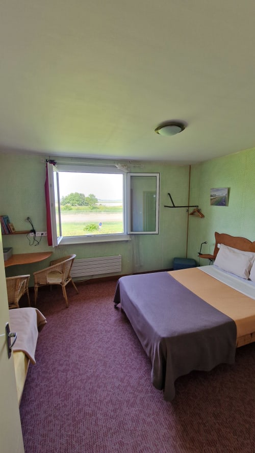 Chambre triple de l'Hôtel Rose avec vue sur la rivière, papier peint vert, mobilier en bois et literie violette à Beauvoir