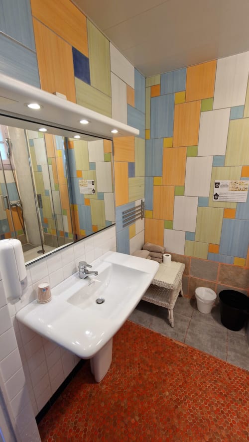Salle de bain moderne de l'Hôtel Rose Beauvoir avec murs en carrelage bois coloré, lavabo blanc, miroir et carreaux hexagonaux rouges au sol
