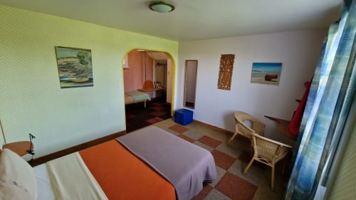 Chambre triple de l'Hôtel Rose à Beauvoir avec vue sur la rivière, literie orange et mauve, chaises en osier et paysage