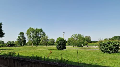 Vastes espaces verts à l'Hôtel Rose à Beauvoir avec arbres matures, pelouse soignée et allées sous un ciel bleu dégagé