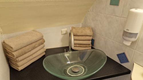 Lavabo de la salle de bain de l'Hôtel Rose avec vasque en verre vert, serviettes beiges et produits d'accueil à Beauvoir, France