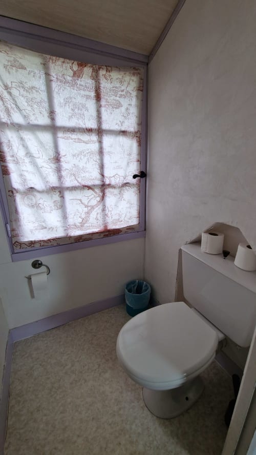 Salle de bain compacte à l'Hôtel Rose à Beauvoir avec toilettes blanches, lavabo sur colonne et fenêtre décorée de motifs floraux