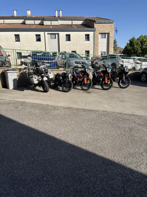 Rangée de motos stationnées à l'Hôtel Du Rocher au Caylar avec des voitures en arrière-plan