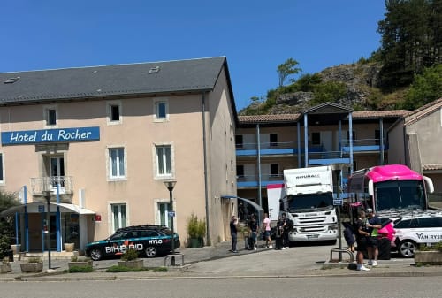 Entrée de l'Hôtel du Rocher à Le Caylar, bâtiment de couleur pêche avec autobus de tourisme stationnés devant