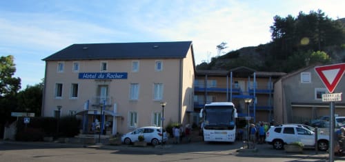 Façade de l'Hôtel du Rocher à Le Caylar, France avec véhicules garés et paysage montagneux
