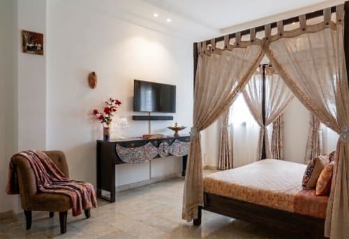 Chambre luxueuse à la Villa Jaddis Abidjan avec lit à baldaquin, TV écran plat, mobilier élégant et rideaux beige