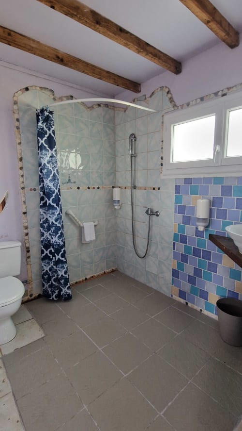 Salle de bain accessible avec douche à l'italienne, carreaux colorés et poutres en bois à l'Hôtel Rose, Beauvoir
