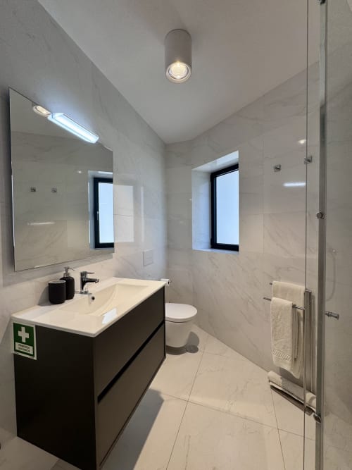 Modern bathroom in RIA CENTRUM Smart Residence, Aveiro with marble walls, black vanity, large mirror, and walk-in shower