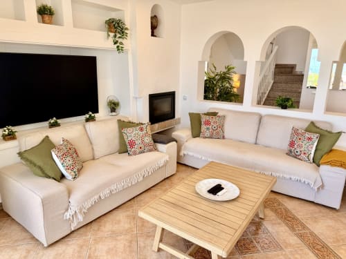 Amplia sala de estar en Villa Sienna, Nerja con dos sofás crema, mesa de café de madera, TV de pantalla plana y arcos