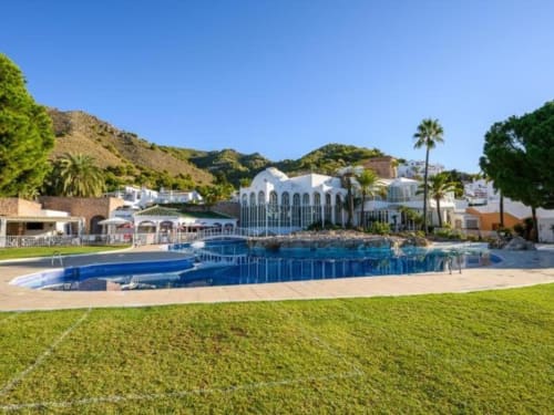 Apartamento de lujo Nerja Holiday Homes con vista al mar, piscina azul, arquitectura blanca, palmeras y ubicación en ladera