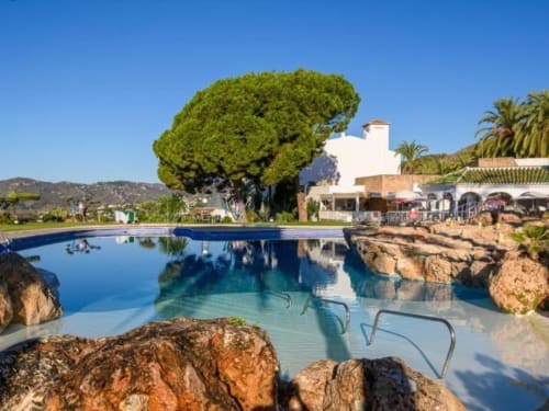 Lujosa piscina en Nerja Holiday Homes con elementos de piedra, edificio blanco, palmeras y vistas al mar en Nerja, España