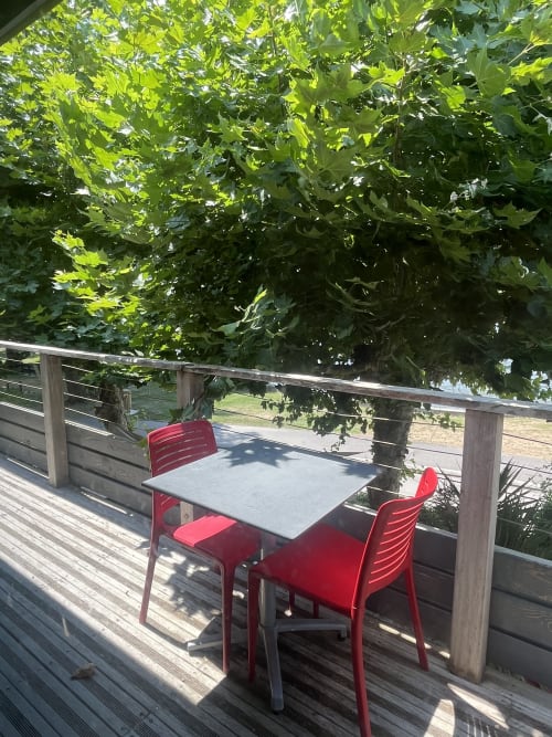 Table de salle à manger extérieure avec chaises rouges sur une terrasse en bois à L'Auberge de la Pointe, Soustons, vue sur le lac et arbres verts