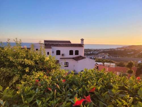 Villa rosa en Nerja con vistas al mar al atardecer, rodeada de flores rojas y paisaje mediterráneo