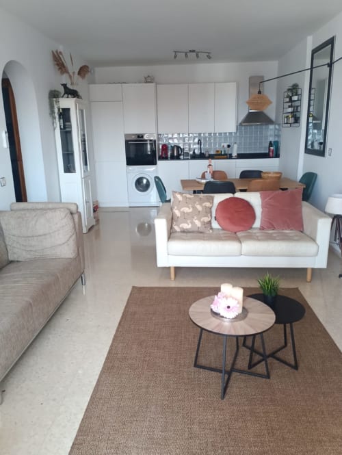 Salón y cocina de concepto abierto en lujoso apartamento de Nerja con sofá blanco, mesa de comedor de madera y diseño contemporáneo