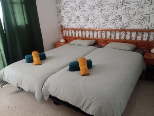 Dos camas gemelas con sábanas blancas y toallas enrolladas en apartamento de lujo Nerja Holiday Homes, cortinas verdes y estampadas