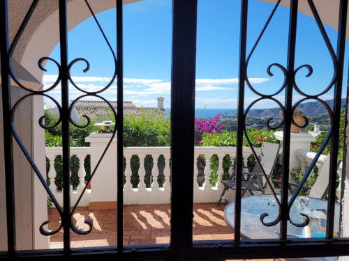 Elegantes puertas de hierro forjado negro que se abren a terraza con vistas a la costa de Nerja y el Mar Mediterráneo