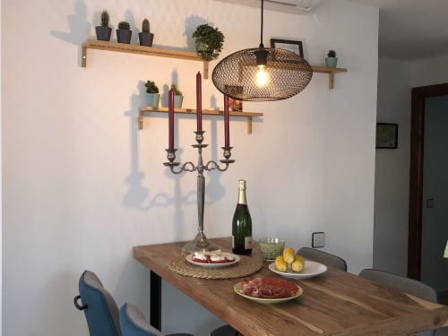 Comedor moderno en Nerja Holiday Homes con mesa de madera, candelabro, vino, aperitivos y plantas en maceta sobre estante flotante