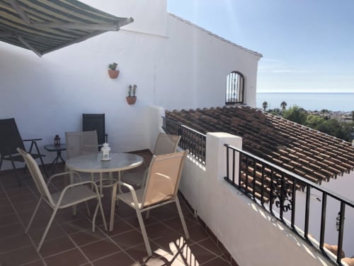 Terraza con vistas al mar en Nerja Holiday Homes, con mesa de comedor, sillas, toldo rayado y paisaje mediterráneo