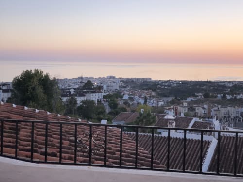 Vista del atardecer desde el balcón de Nerja Holiday Homes con vistas a la costa mediterránea, tejados de barro y horizonte marino