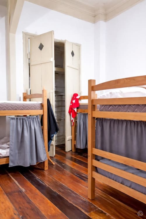 Quarto misto com beliches de madeira e cortinas cinzas no Rio Vibes Hostel no Rio de Janeiro