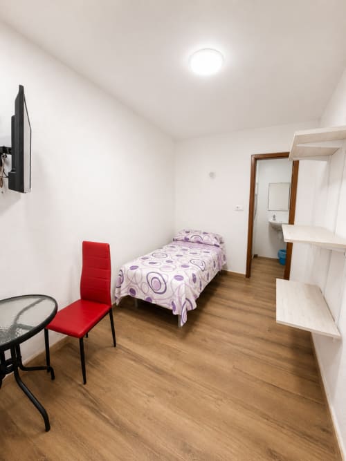 Habitación individual en Hostal Europa de Aldaia con cama, silla roja, TV, suelo de madera y estantería blanca