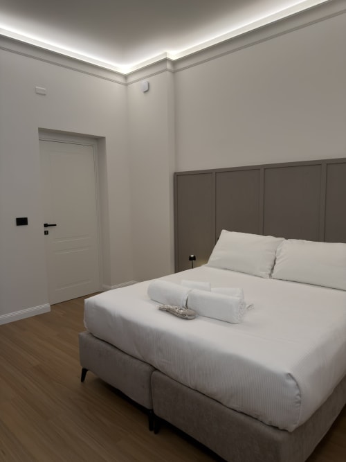 Camera moderna a Maison Riviera a Reggio di Calabria con letto queen, testata grigia, biancheria bianca e parquet