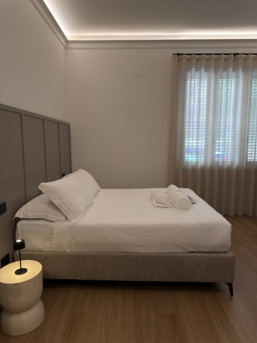 Camera moderna a Maison Riviera con biancheria bianca, struttura letto grigia e tende trasparenti a Reggio di Calabria
