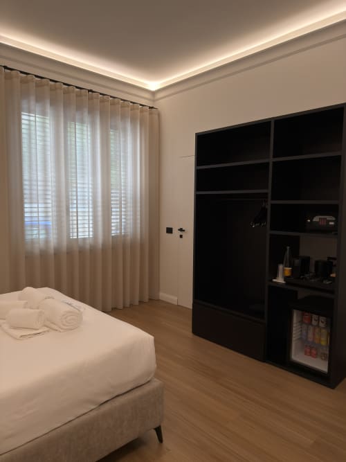 Camera moderna a Maison Riviera con letto bianco, tende trasparenti, mobile nero con minibar e pavimento in legno