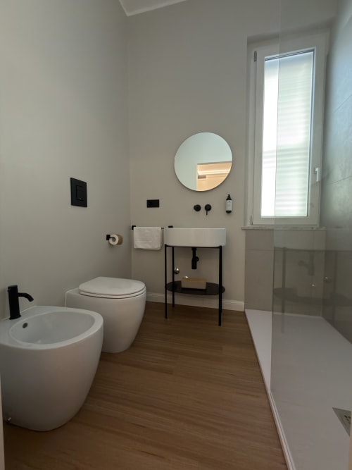 Bagno moderno a Maison Riviera con wc, bidet, specchio rotondo, lavabo e doccia walk-in a Reggio di Calabria