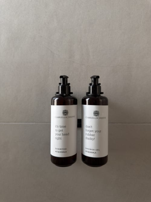 Due bottiglie scure di cosmetici Gabriella Chieffo con etichette giocose per shampoo e bagnoschiuma a Maison Riviera