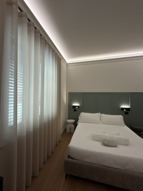 Camera da letto moderna presso Maison Riviera Reggio di Calabria con tende trasparenti, testata verde e luci ambientali a soffitto