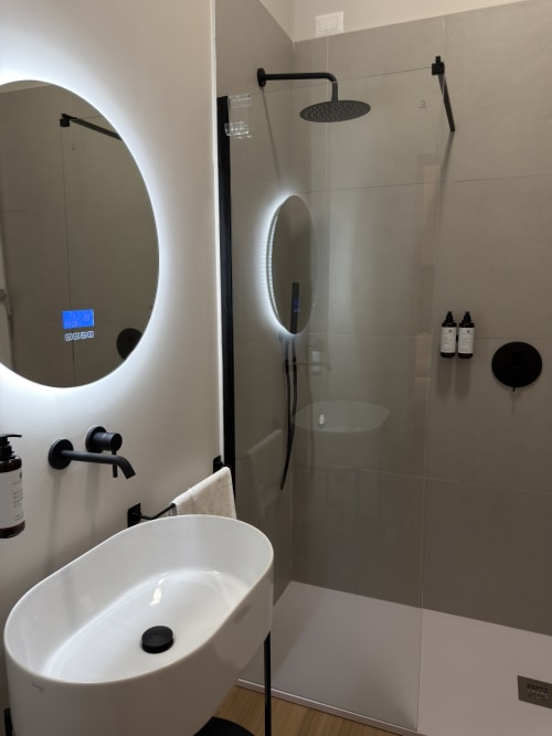 Bagno moderno di Maison Riviera a Reggio di Calabria con specchio ovale illuminato, lavabo bianco e dettagli neri