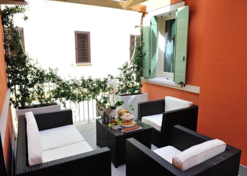 Zona sedute in terrazza a La Finestra sul porto a Cesenatico con mobili in vimini nero, cuscini bianchi e piante in vaso
