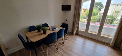 Salle à manger moderne avec table en bois, chaises noires, télévision et vue sur le jardin à l'appartement Terrasses des Lecques près de Lecques
